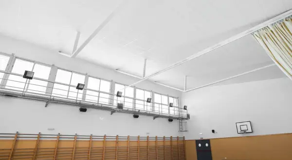 Techo de gimnasio con falso techo Heraklith, ventanas altas, canasta de baloncesto y equipamiento deportivo.