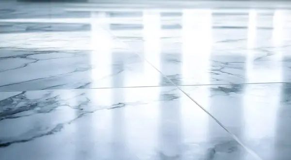 Suelo de mármol pulido con vetas grises. La luz se refleja intensamente, mostrando que el mármol es poroso y absorbe la humedad.