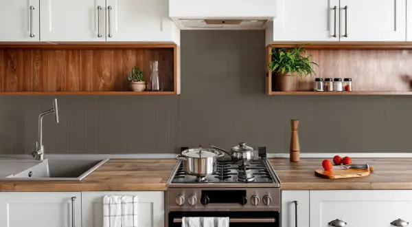 Cocina moderna con pared mitad azulejo gris y mitad estante de madera. Ollas en la estufa, grifo y plantas decorativas.