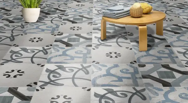 Un suelo hidráulico con un diseño de azulejos en tonos grises y azules, con un pequeño taburete de madera y una planta. ¡Perfecto para limpiar y lucir!
