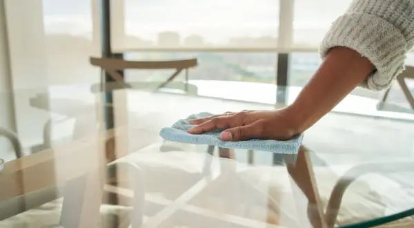 Mano limpiando una mesa de cristal, eliminando los cristales opacos para dejarla reluciente.