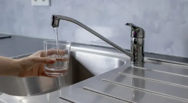 Un vaso se llena de agua bajo un grifo moderno, mostrando la buena presión del agua del grifo.