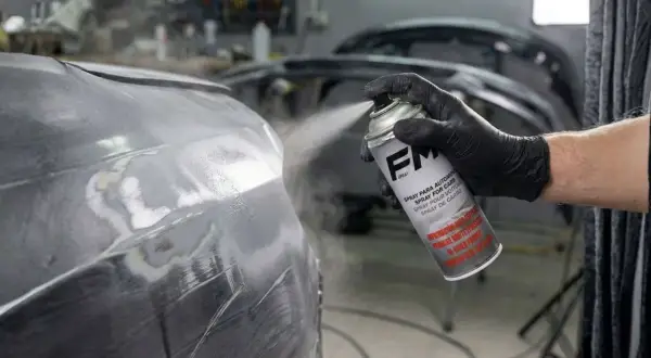 Mano enguantada aplica imprimación en spray a un coche. Se puede dar imprimación encima de pintura para un acabado perfecto.