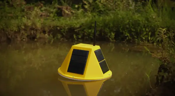 Boya amarilla con paneles solares y antena flotando en agua turbia, parte de un sistema de control de nivel de agua.