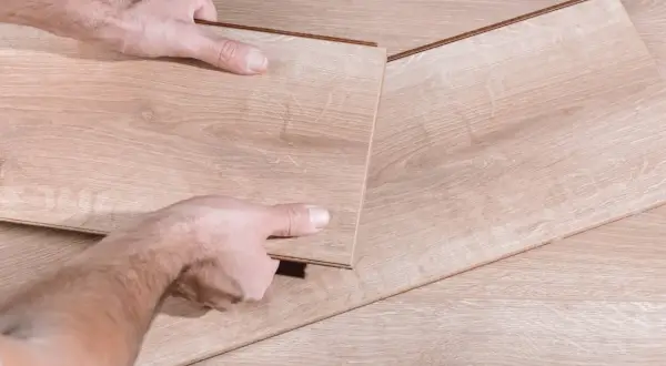 Man's hands fitting a new laminate plank to replace damaged parquet.