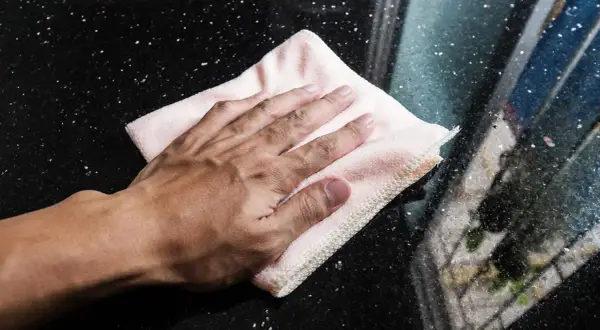 Mano limpiando manchas de humedad en mármol negro con un paño rosa.