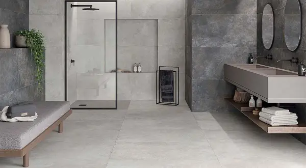 Baño moderno con ducha, lavabo doble y banco. Paredes y suelo revestidos con elegante material gres en tonos grises y oscuros.