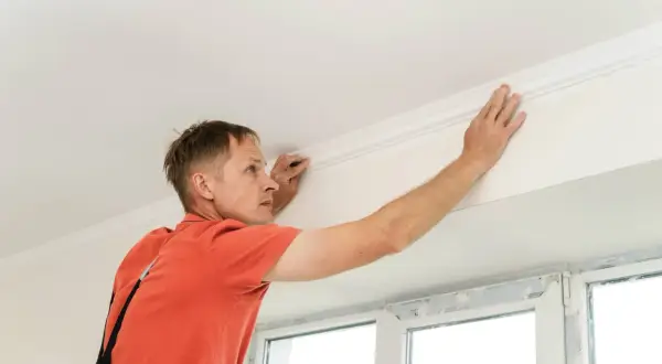 Hombre instalando moldura de escayola en el techo. Aprende como hacer escayola para techo y embellece tu hogar.
