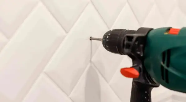 Taladro perforando azulejo blanco. Aprende cómo tapar agujeros en azulejos para un acabado perfecto.