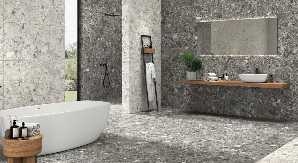 Baño moderno con bañera exenta y lavabo sobre encimera. Las paredes y el suelo muestran diferentes tipos de azulejos con efecto terrazo en tonos grises.