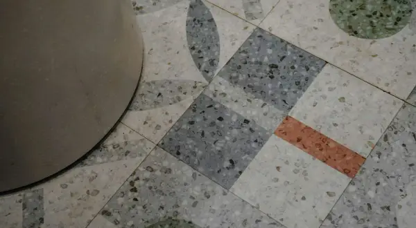 Detalle de un suelo terrazo con diseño geométrico y un pilar. El pulido del suelo terrazo resalta sus motas de colores.