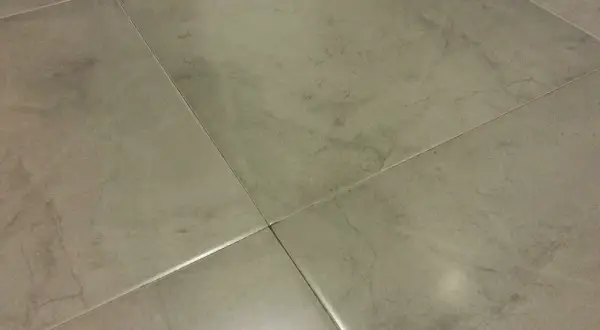 Detalle de la colocación de cerámica gris en un suelo, mostrando las juntas finas y el acabado mate.