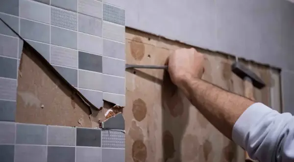 Persona usando un cincel para quitar juntas de azulejos viejos y dañados de una pared.
