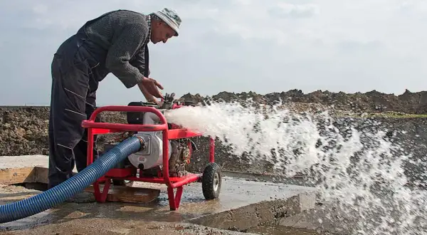 Hombre trabajando con una bomba de agua que lanza un chorro potente. A pesar de que se puede andar con la bomba de agua rota, él la mantiene en funcionamiento.
