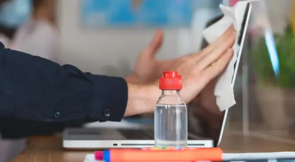 Un hombre limpia la pantalla de su portátil con un paño. Una botella de alcohol de limpieza está al lado, mostrando para que sirve el alcohol de limpieza: desinfectar.