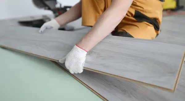 Manos enguantadas instalando suelos gran formato de madera gris.