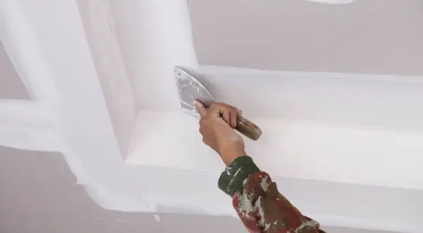 Mano aplica masilla con espátula en el techo, como quitar escayola del techo.