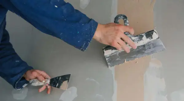 Man alicatando sobre pladur, alisando la pared con una llana.