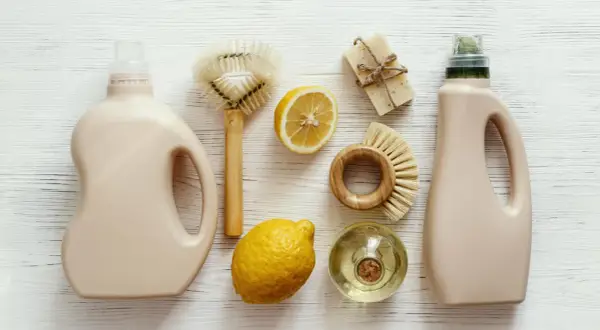 Dos botellas de detergente, jabón, limones y cepillos de madera para una limpieza sostenible.