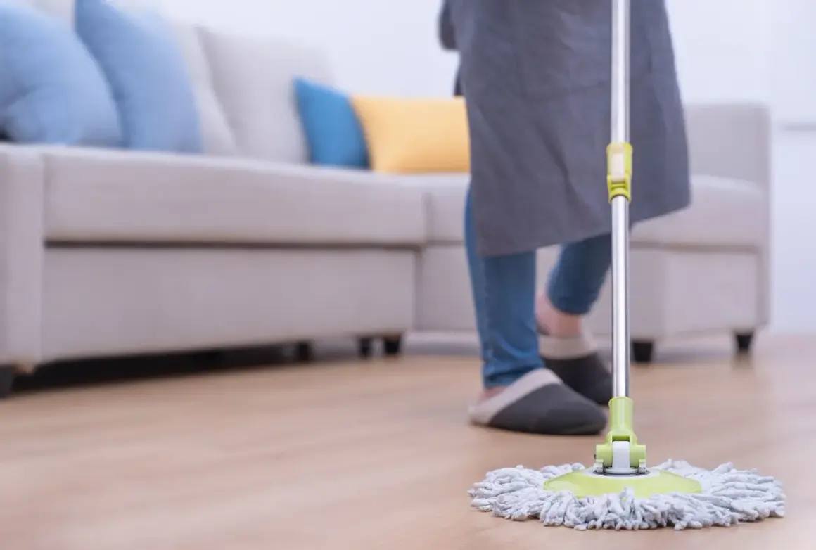 Persona con delantal y zapatillas limpiando el suelo con una mopa. Aprende como limpiar la mopa después de usarla para mantener tu hogar impecable.