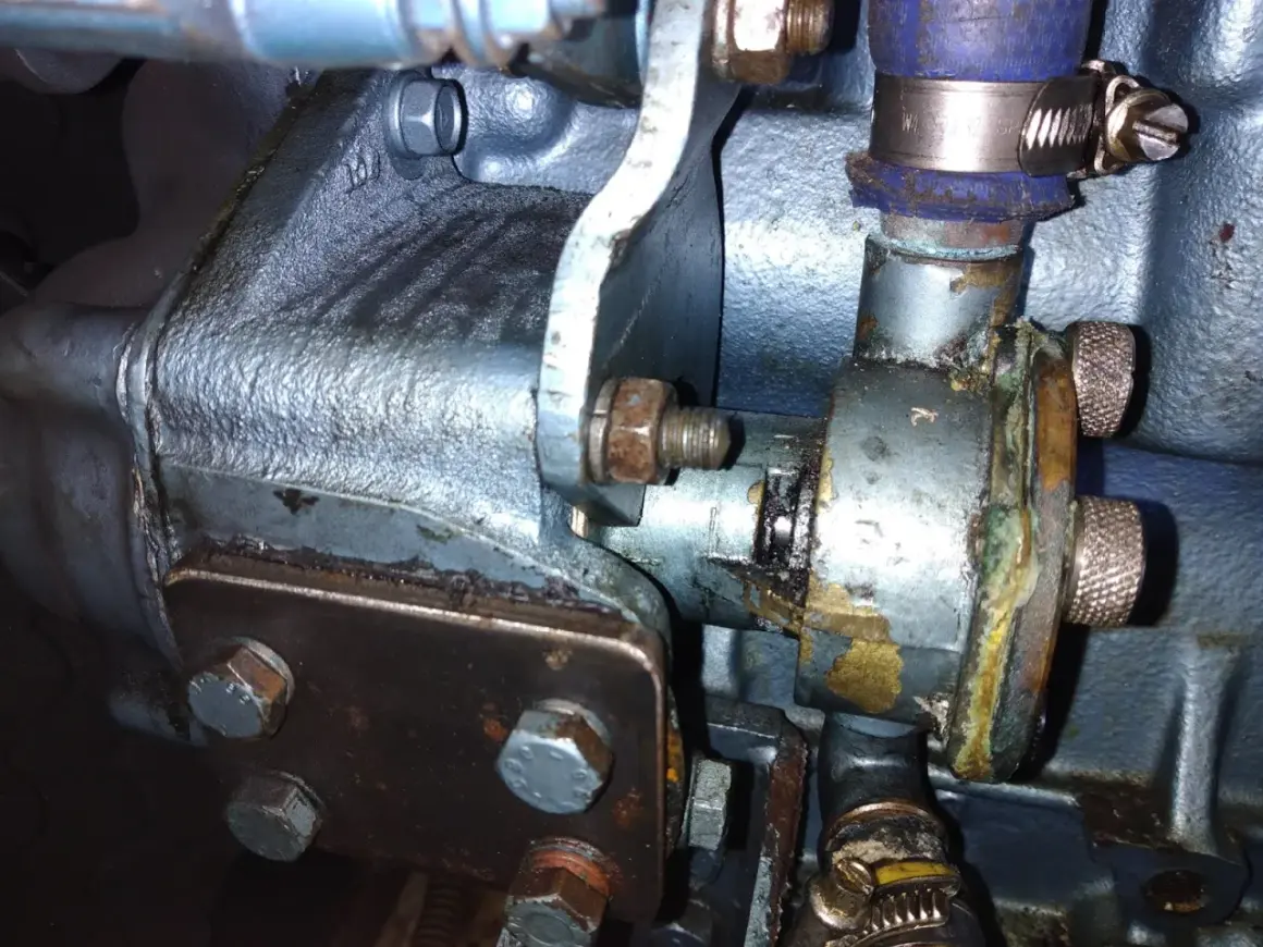 Detalle de una bomba de agua que pierde agua, con óxido y corrosión visibles en sus componentes metálicos y mangueras.
