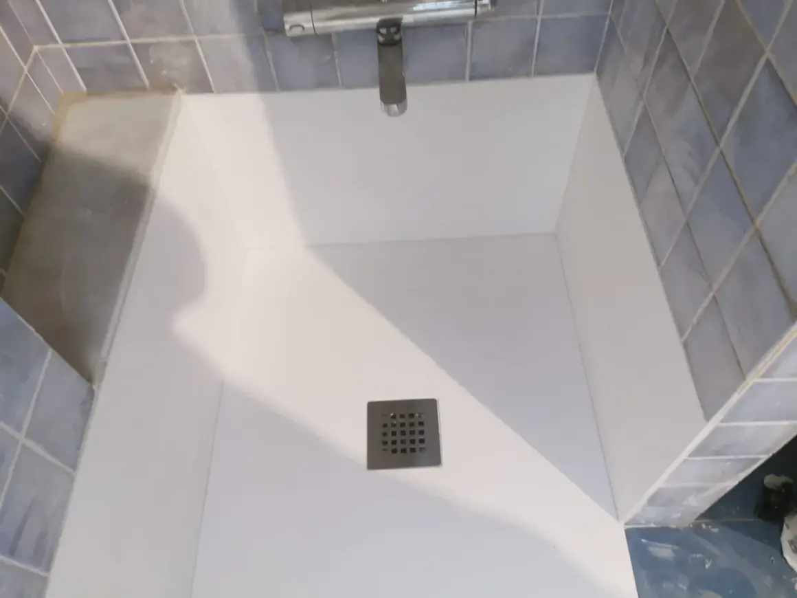 Instalación de un nuevo plato de ducha blanco, con azulejos azules y grifería cromada.