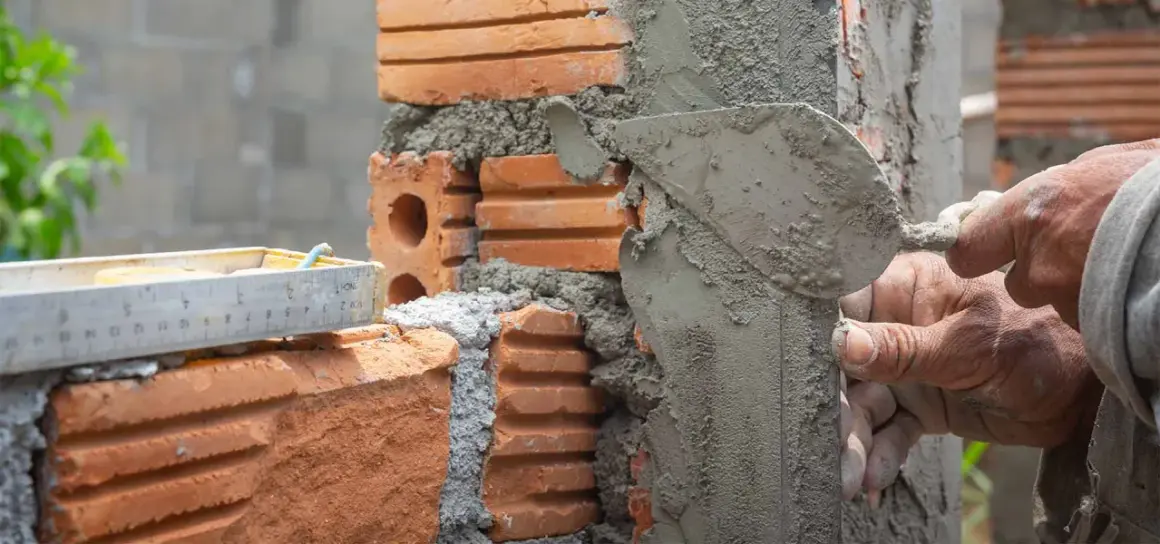 Man applying mezcla para pegar ladrillos con una paleta. Se ve una regla de albañil.