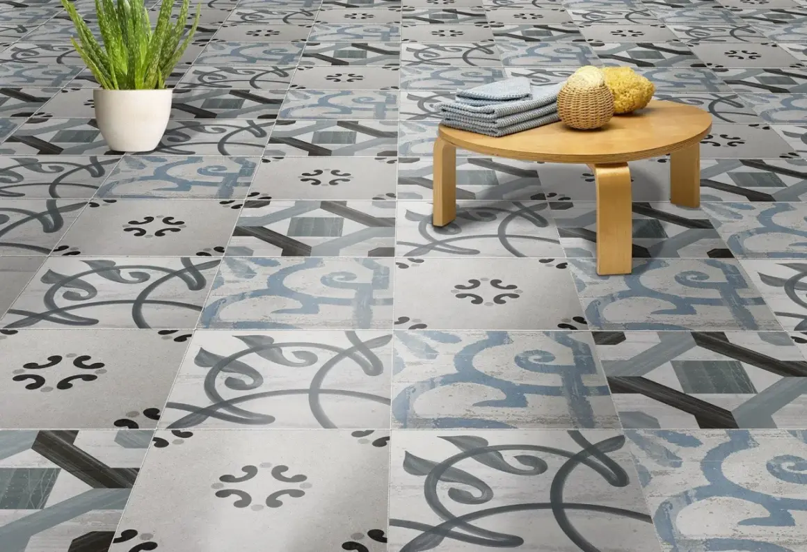Un suelo hidráulico con un diseño de azulejos en tonos grises y azules, con un pequeño taburete de madera y una planta. ¡Perfecto para limpiar y lucir!