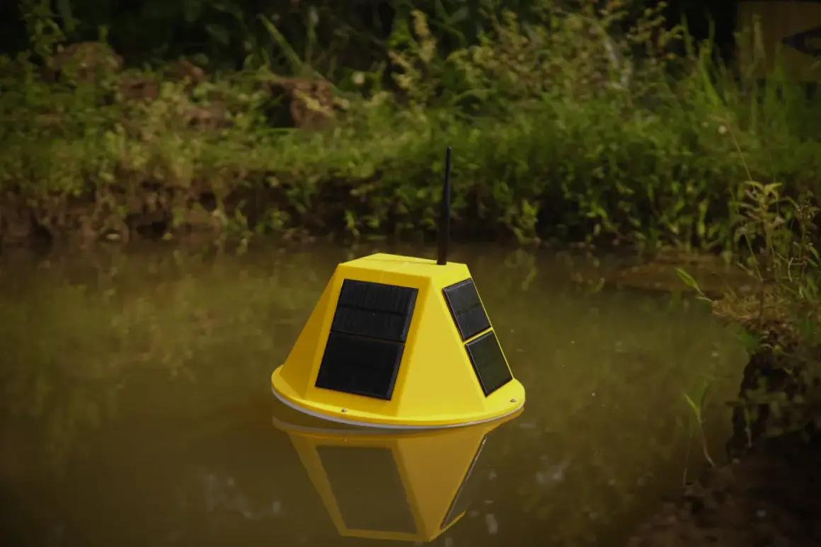 Boya amarilla con paneles solares y antena flotando en agua turbia, parte de un sistema de control de nivel de agua.