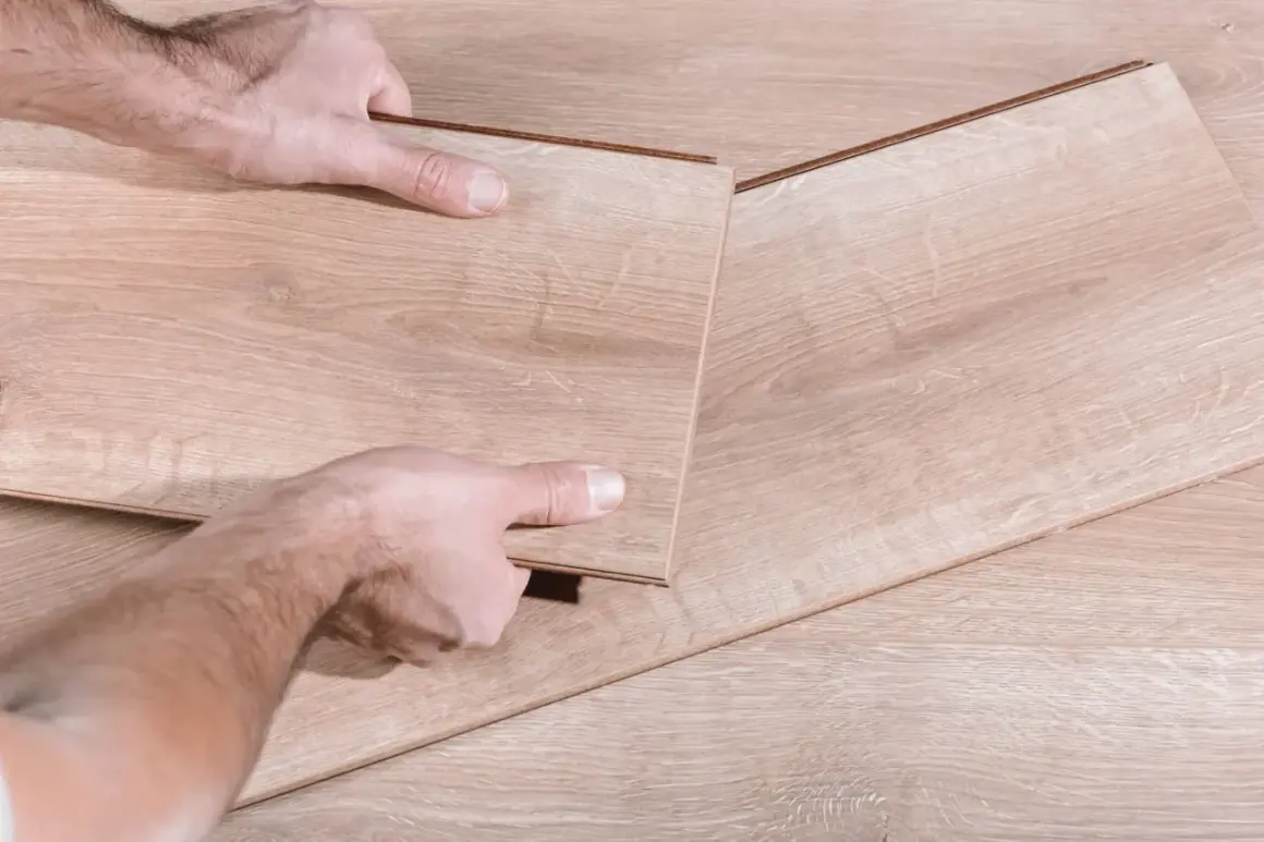 Man's hands fitting a new laminate plank to replace damaged parquet.