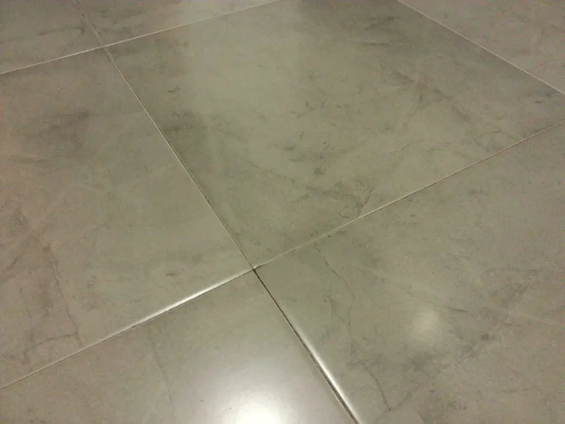 Detalle de la colocación de cerámica gris en un suelo, mostrando las juntas finas y el acabado mate.
