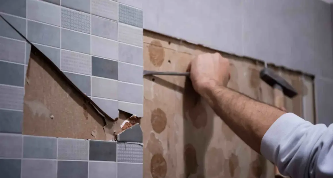 Persona usando un cincel para quitar juntas de azulejos viejos y dañados de una pared.