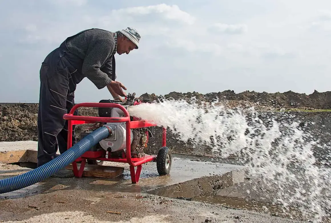 Hombre trabajando con una bomba de agua que lanza un chorro potente. A pesar de que se puede andar con la bomba de agua rota, él la mantiene en funcionamiento.
