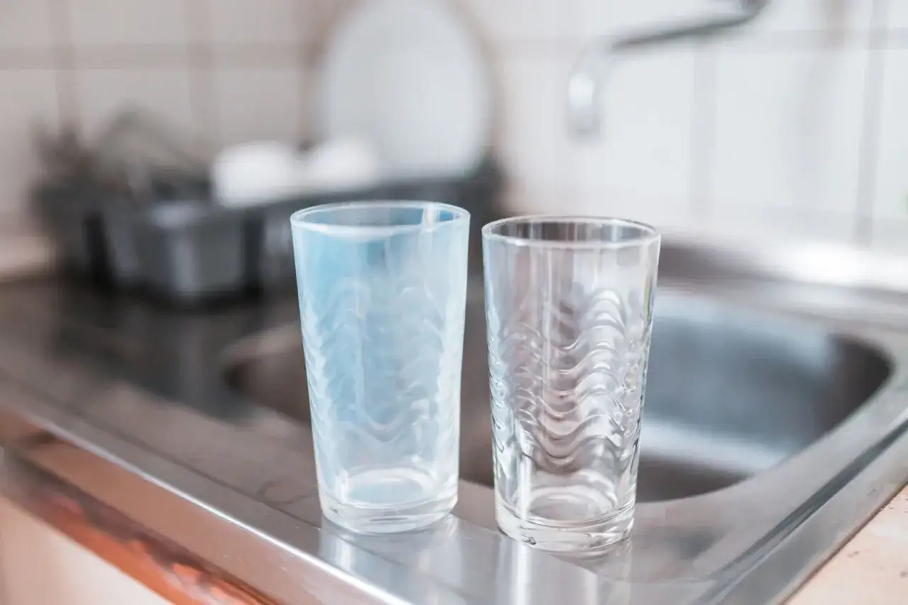 Dos vasos, uno con cristales opacos y otro transparente, junto a un fregadero.