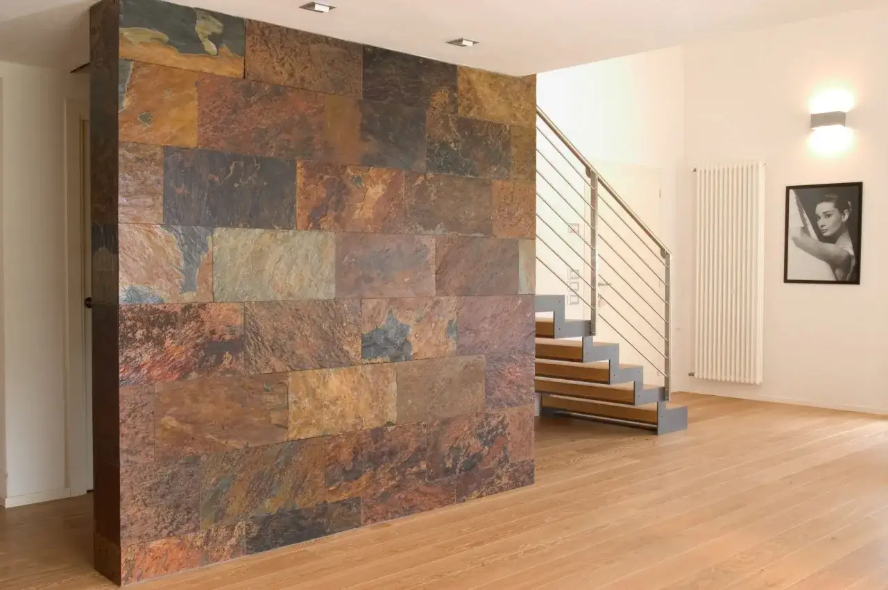 Una pared revestida con baldosas de pizarra en tonos tierra, creando un dise&ntilde;o r&uacute;stico y moderno. Ideal para quienes buscan ideas sobre como revestir una pared con estilo.