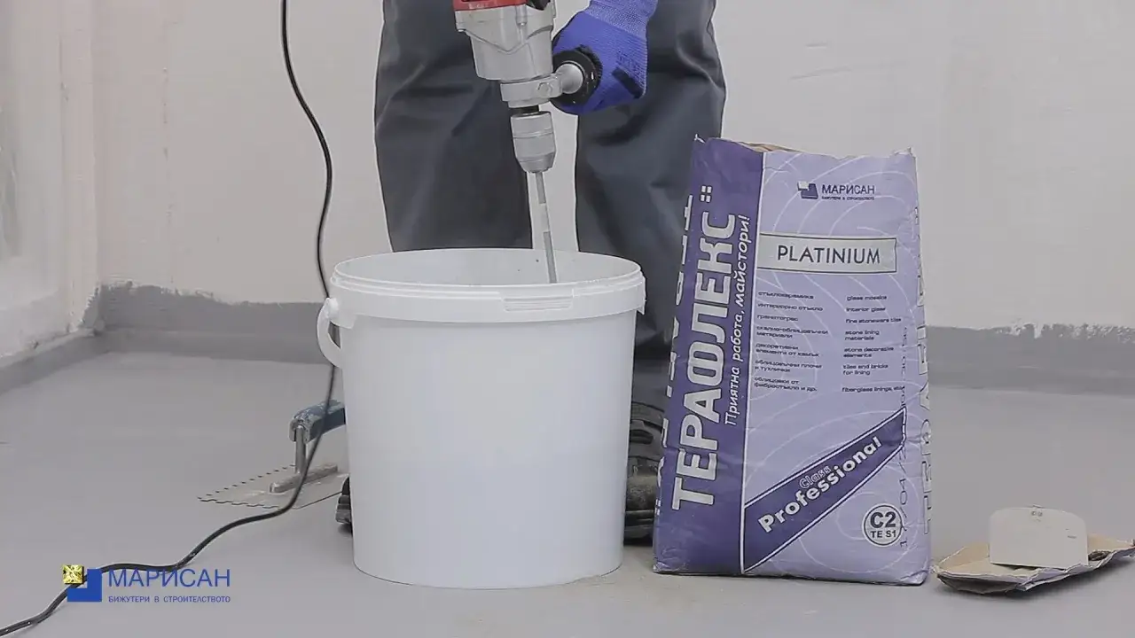 Preparando cemento cola para poner azulejos. Un mezclador el&eacute;ctrico remueve la mezcla en un cubo blanco junto a un saco de 
