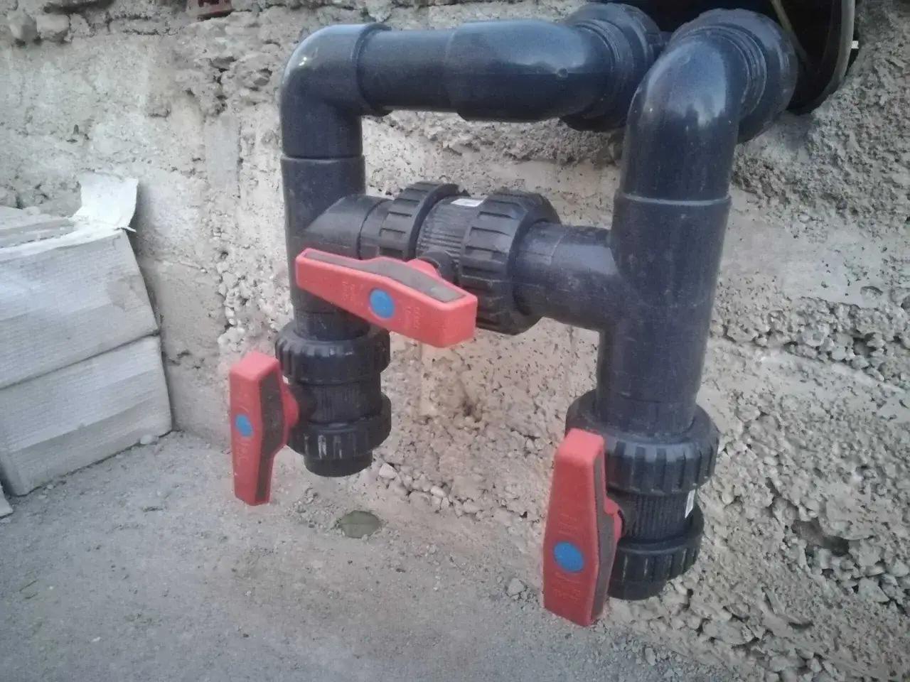 Instalación de bypass para bomba de agua con válvulas rojas y tuberías negras.