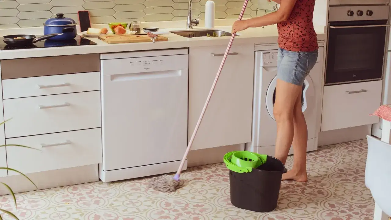Persona friega el suelo de la cocina con una mopa, aprendiendo como quitar la grasa del suelo de la cocina.
