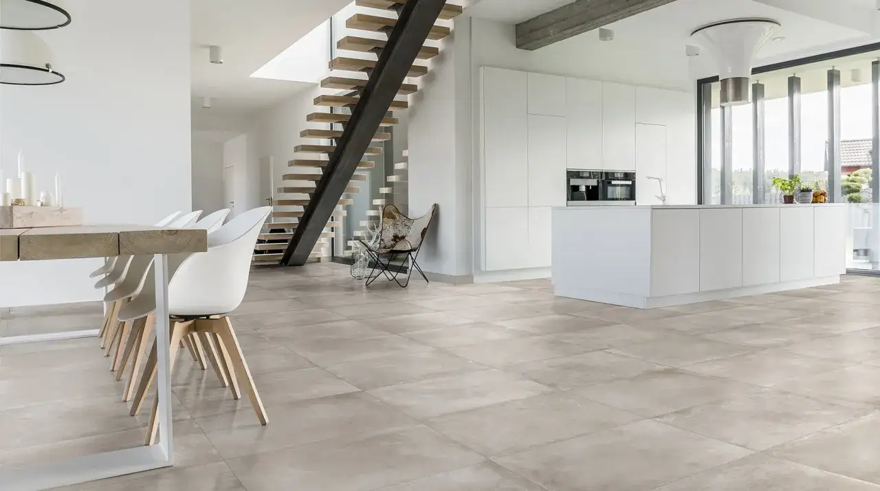 Amplio sal&oacute;n comedor con cocina moderna y escaleras flotantes, todo sobre elegantes suelos gran formato de tonos neutros.