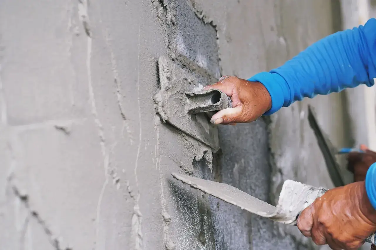 Manos expertas aplican mortero a una pared con una llana. El mortero que es, se ve fresco y listo para dar forma.