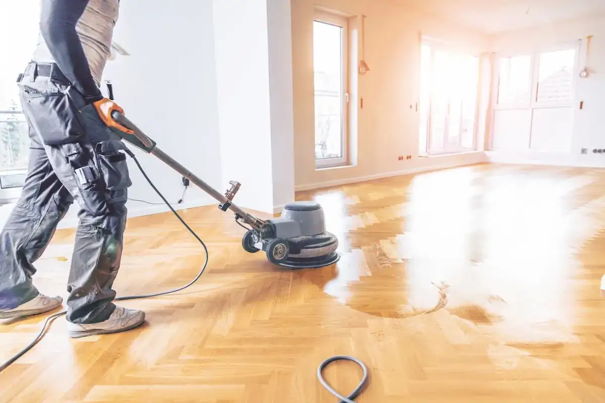 Profesional puliendo parquet para eliminar manchas. El suelo de madera recupera su brillo.
