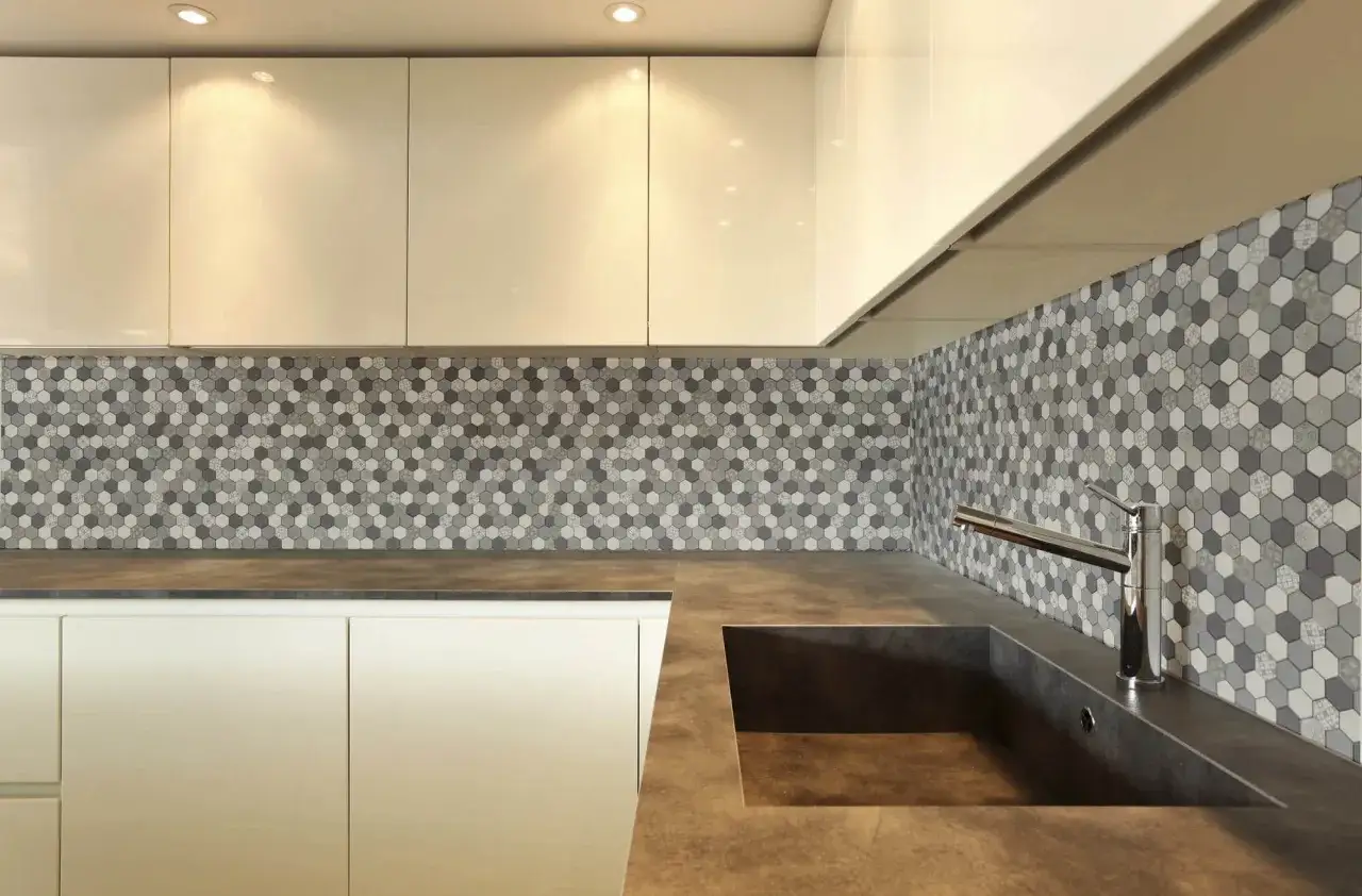 Encantadores mosaicos de azulejos hexagonales en tonos grises y blancos adornan la pared de la cocina, creando un patr&oacute;n moderno y elegante.