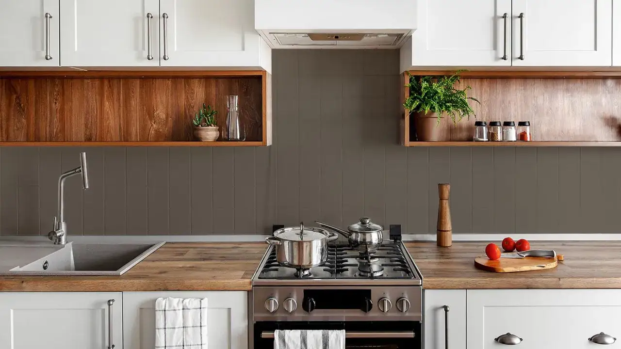 Pared de cocinas con mitad azulejo gris y mitad pintura. Encimeras de madera, fregadero, cocina de gas con ollas y tabla de cortar con tomates.