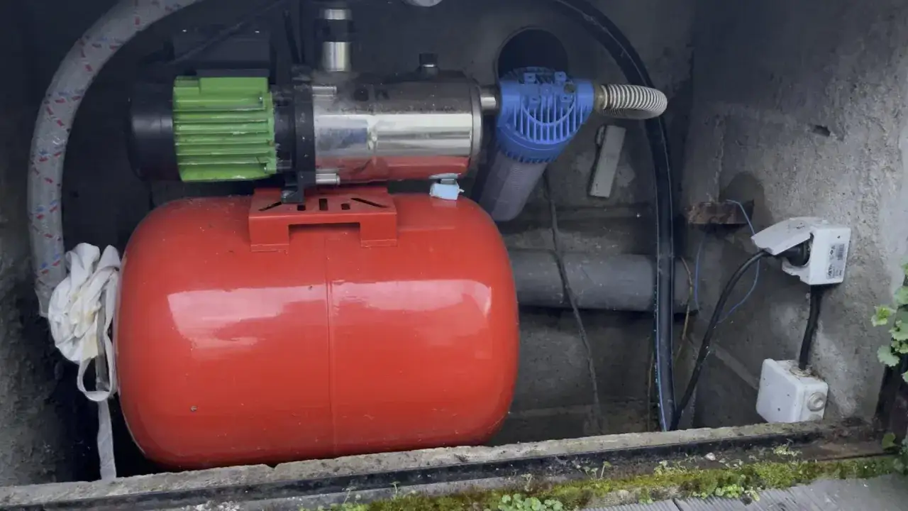 Bomba de agua funciona intermitente: motor verde, tanque rojo, filtro azul y conexiones el&eacute;ctricas en un pozo.