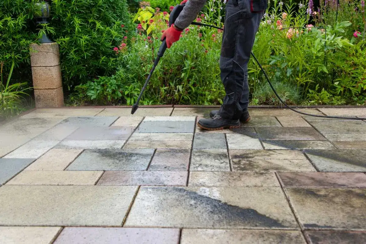 Persona usa hidrolimpiadora para quitar manchas grasa suelo terraza.