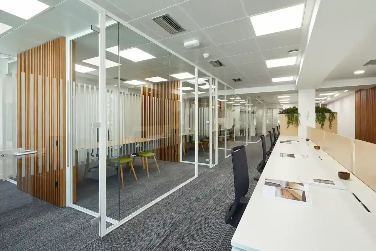 Oficina moderna con mamparas de cristal, paredes de lamas de madera y techos registrables iluminados.