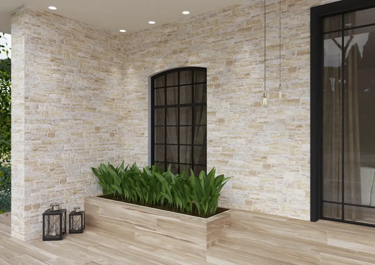 Pared de material gres con textura de piedra, ventana arqueada y macetero con plantas verdes.