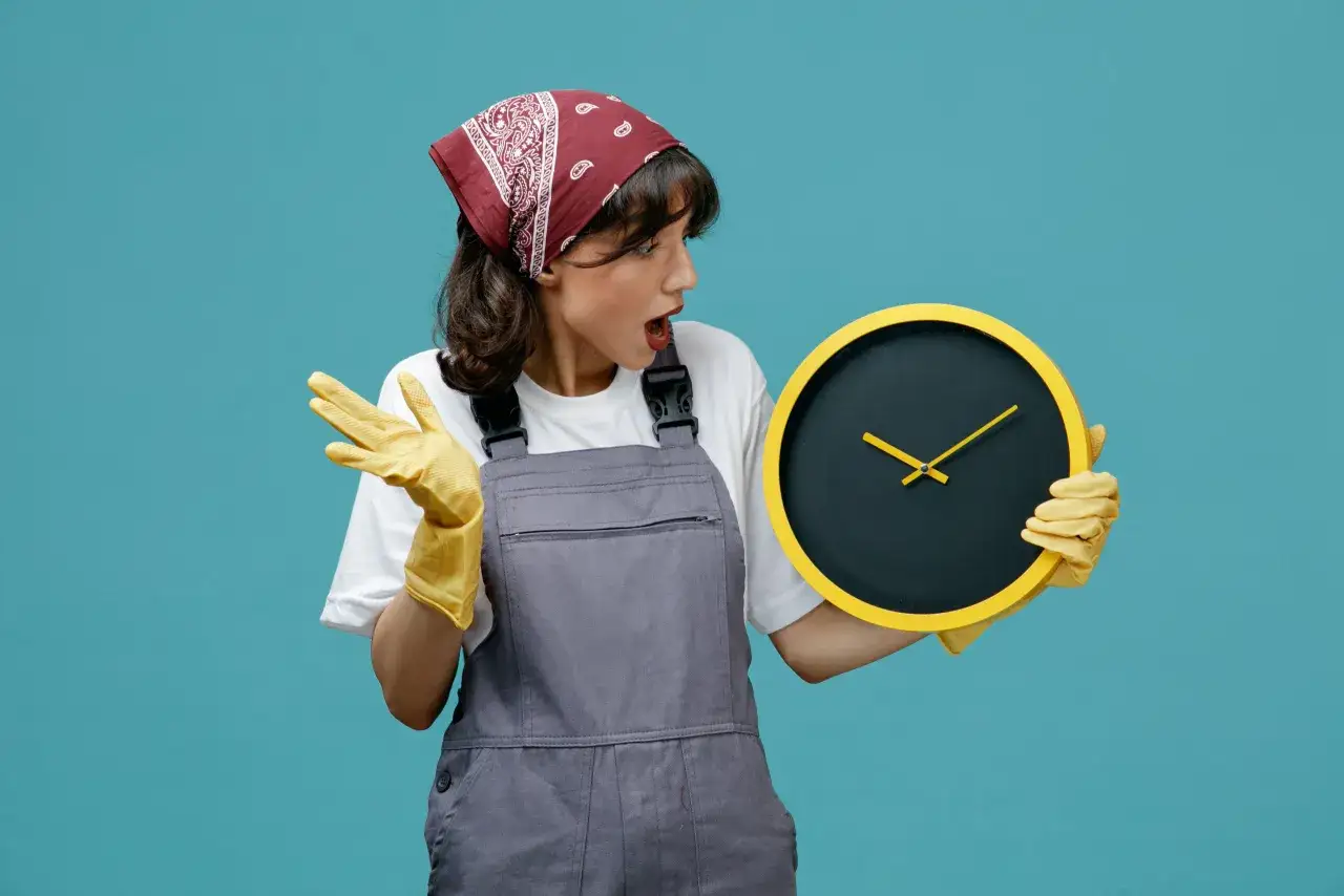Mujer con mono de trabajo y guantes amarillos, sorprendida por el tiempo en un reloj. &iexcl;Descubre trucos para limpiar la casa a fondo sin perder tiempo!