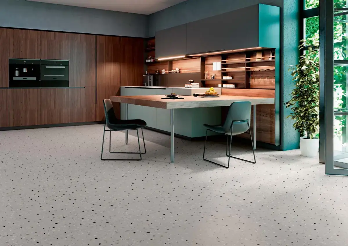 Cocina moderna con armarios de madera oscura y encimeras grises. El suelo de terrazo claro con motas oscuras aporta un toque contempor&aacute;neo.