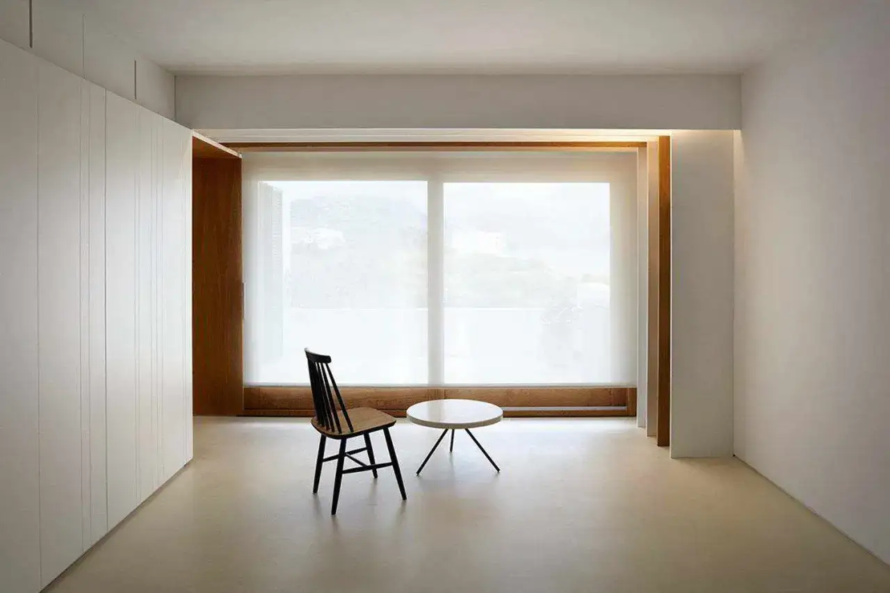 Habitaci&oacute;n minimalista con suelo de microcemento, armario blanco y ventana panor&aacute;mica.